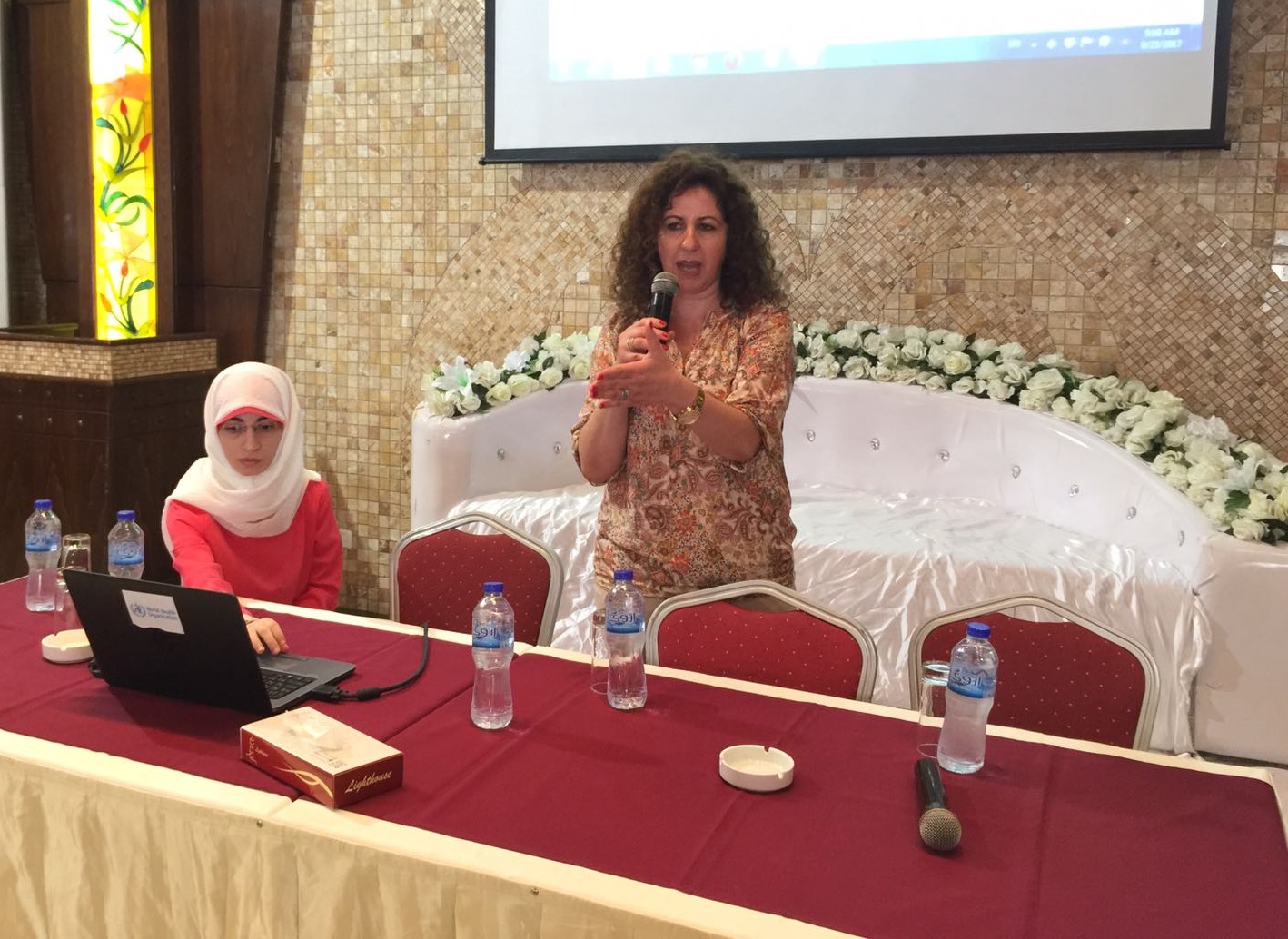 one person sitting at a table and another person talking into microphone